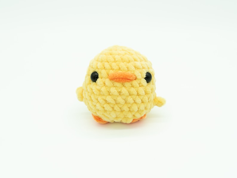 May include: A yellow crocheted chick toy with black eyes and an orange beak.
