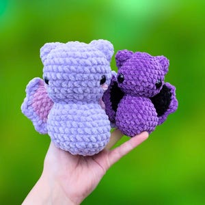 K&ouml;nnte beinhalten: Zwei geh&auml;kelte Pl&uuml;sch-Fledermausspielzeuge. Die gr&ouml;&szlig;ere Fledermaus ist helllila mit rosa Fl&uuml;geln. Die kleinere Fledermaus ist dunkelviolett mit schwarzen Fl&uuml;geln.