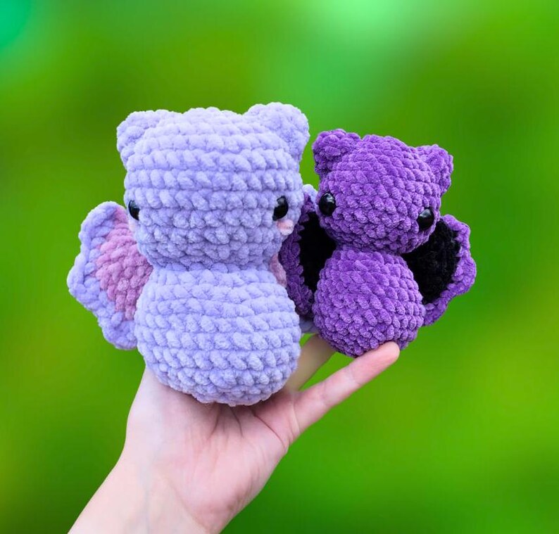 K&ouml;nnte beinhalten: Zwei geh&auml;kelte Pl&uuml;sch-Fledermausspielzeuge. Die gr&ouml;&szlig;ere Fledermaus ist helllila mit rosa Fl&uuml;geln. Die kleinere Fledermaus ist dunkelviolett mit schwarzen Fl&uuml;geln.
