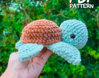 May include: A crocheted turtle amigurumi toy with a brown shell and light blue body. The toy has black eyes and is held in a hand. The image includes the text "PDF PATTERN".
