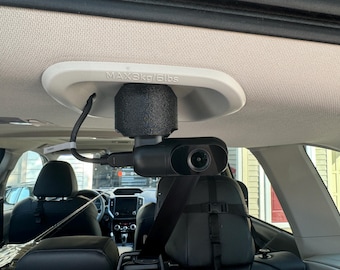May include: A black dashcam mounted to the ceiling of a car with a white mounting plate that says "MAX 3kg/6lbs". The camera is pointed towards the back seat.