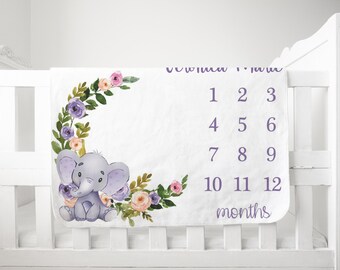 Könnte beinhalten: Eine weiße Baby-Meilenstein-Decke mit einem violetten Blumenkranz und einer grauen Elefantenillustration. Die Decke hat die Zahlen 1-12 darauf gedruckt, mit dem Text "Monate" unter den Zahlen.