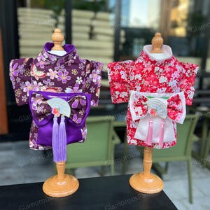 以下が含まれることがあります： 木製のスタンドに置かれた2つの犬用着物。1つは紫色の花柄とマッチするリボン。もう1つは赤い花柄と白いリボン。どちらも装飾的な扇子とタッセルが付いています。