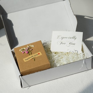 Op de afbeelding: Een witte cadeaudoos met een bruine doos erin. De bruine doos heeft een klein boeket witte en roze bloemen en een label met de tekst "handgemaakt met" met een rood hart. De witte doos heeft een witte kaart erin met de tekst "Speciaal voor jou".