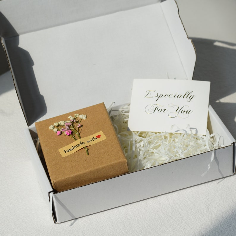 Op de afbeelding: Een witte cadeaudoos met een bruine doos erin. De bruine doos heeft een klein boeket witte en roze bloemen en een label met de tekst "handgemaakt met" met een rood hart. De witte doos heeft een witte kaart erin met de tekst "Speciaal voor jou".