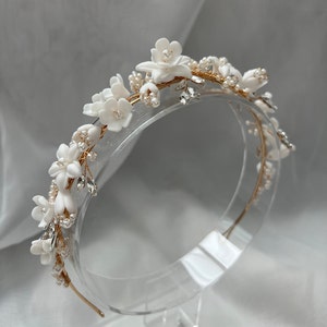 May include: A gold headband with white floral accents and pearl beads. The headband is decorated with small white flowers and pearl beads, creating a delicate and elegant look.