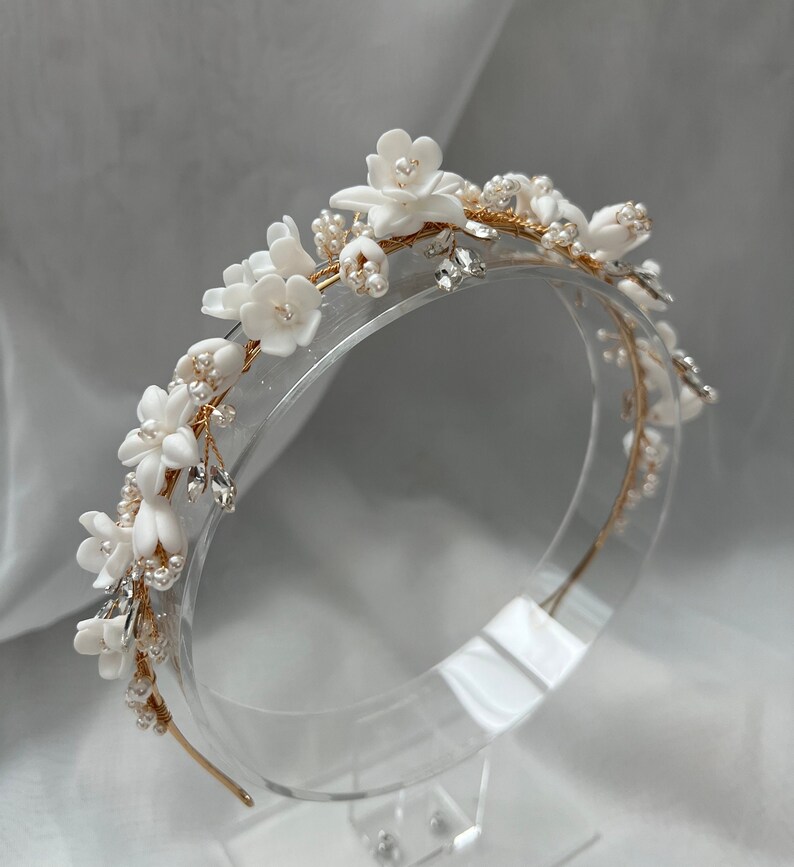 May include: A gold headband with white floral accents and pearl beads. The headband is decorated with small white flowers and pearl beads, creating a delicate and elegant look.