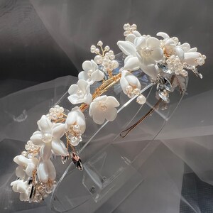May include: A white floral headband with pearl and crystal accents. The headband is made of gold wire and has a delicate, feminine design.