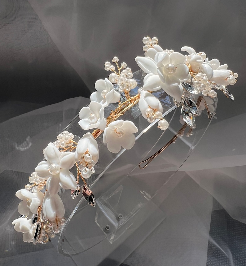 May include: A white floral headband with pearl and crystal accents. The headband is made of gold wire and has a delicate, feminine design.