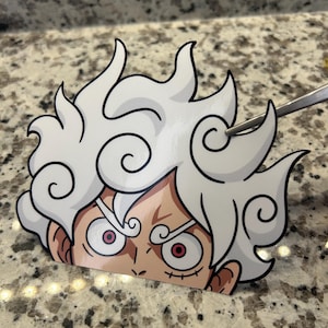 Puede incluir: Una pegatina troquelada que representa a un personaje con pelo blanco y puntiagudo y ojos rojos. La cara del personaje es visible, con una expresión intensa. La pegatina tiene un contorno negro y probablemente sea de una serie de anime o manga.