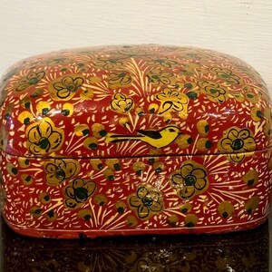 May include: A red, rectangular box with a hinged lid, adorned with a floral and bird design. The box features gold and white floral patterns and a yellow bird. The box is likely made of wood and has a glossy finish.