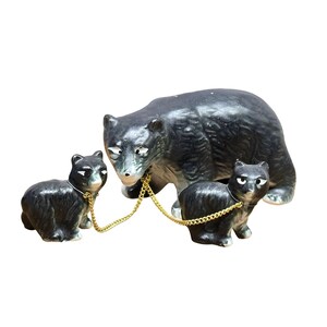 May include: A ceramic figurine set featuring a large black bear and two smaller black bear cubs. The cubs are connected to the larger bear by thin gold-colored metal chains attached to their necks. Each bear has white painted eyes and snout.