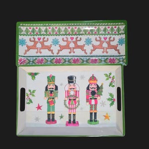 May include: Rectangular serving tray with a green border and a matching lid. The tray features three nutcracker figures and festive holiday patterns. The lid displays reindeer and floral designs.