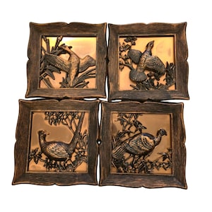May include: A set of four square wall plaques featuring dark brown wood-toned frames and metallic copper-colored centers. Each plaque displays a raised relief sculpture of a different bird in a natural setting with foliage and branches.