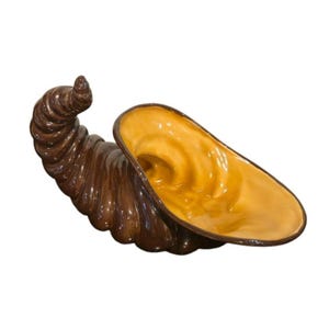 May include: A ceramic cornucopia in a glossy finish. The exterior is a dark brown, while the interior is a warm yellow-orange. The horn-shaped vessel is designed with a curved, spiraling form.