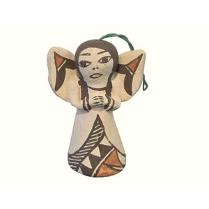 May include: A hand-painted ceramic angel ornament with a cream-colored body, brown hair, and wings. The angel's dress features geometric patterns in black, brown, and orange. A green string is attached for hanging. This decorative item is suitable for holiday decor.