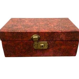 May include: A rectangular storage box featuring a vibrant red base color with a dark, intricate, repeating floral pattern across the entire surface. The box includes a metallic gold-toned latch mechanism centered on the front panel for closure.