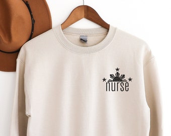 May include: A beige sweatshirt with a black graphic of the Philippine sun and stars with the word "nurse" underneath.