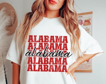 May include: White t-shirt with the word "ALABAMA" in red block letters repeated five times. The word "alabama" is written in a cursive font in the center of the design. The shirt is a casual, oversized style.