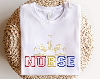May include: White t-shirt with a gold sun and stars design and the word "NURSE" in red, yellow, and blue.