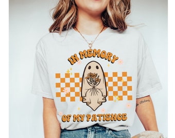Könnte beinhalten: Weißes T-Shirt mit einem Geist, der Blumen hält, und dem Text "In Memory of My Patience" in orangefarbenen und gelben Buchstaben auf einem karierten Hintergrund.