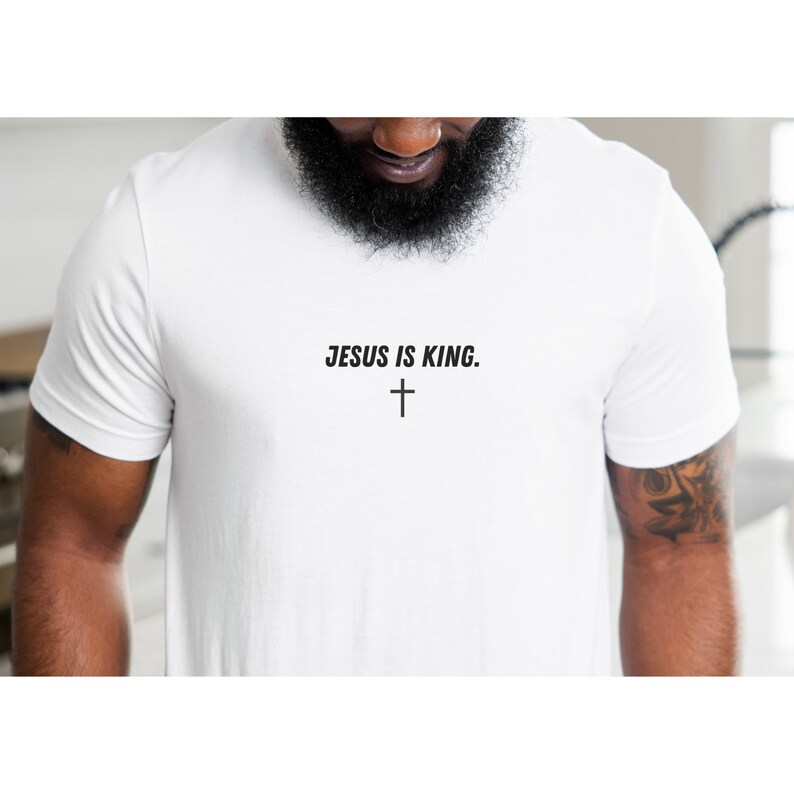 K&ouml;nnte beinhalten: Wei&szlig;es T-Shirt mit dem Text "JESUS IS KING." in Schwarz, zusammen mit einem schwarzen Kreuzsymbol. Das Shirt besteht aus einem weichen Material und ist f&uuml;r den t&auml;glichen Gebrauch geeignet.