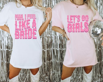 Può includere: Due magliette bianche con testo rosa. La prima maglietta dice "Man, I feel like a bride". La seconda maglietta dice "Let's go girls".