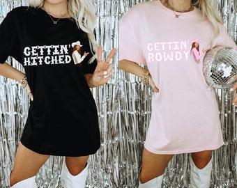 Puede incluir: Dos mujeres con camisetas de gran tamaño. La camiseta negra dice "Gettin' Hitched" y la camiseta rosa dice "Gettin' Rowdy". Ambas camisetas tienen una vaquera de dibujos animados.
