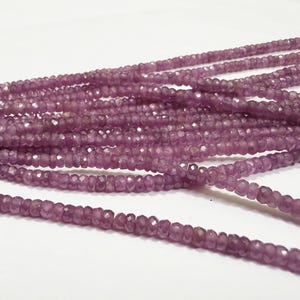 May include: A long strand of small, faceted, round, purple gemstone beads. The beads are uniform in size and shape, featuring a translucent quality with a reflective, multi-faceted surface that catches light across the entire length of the string.