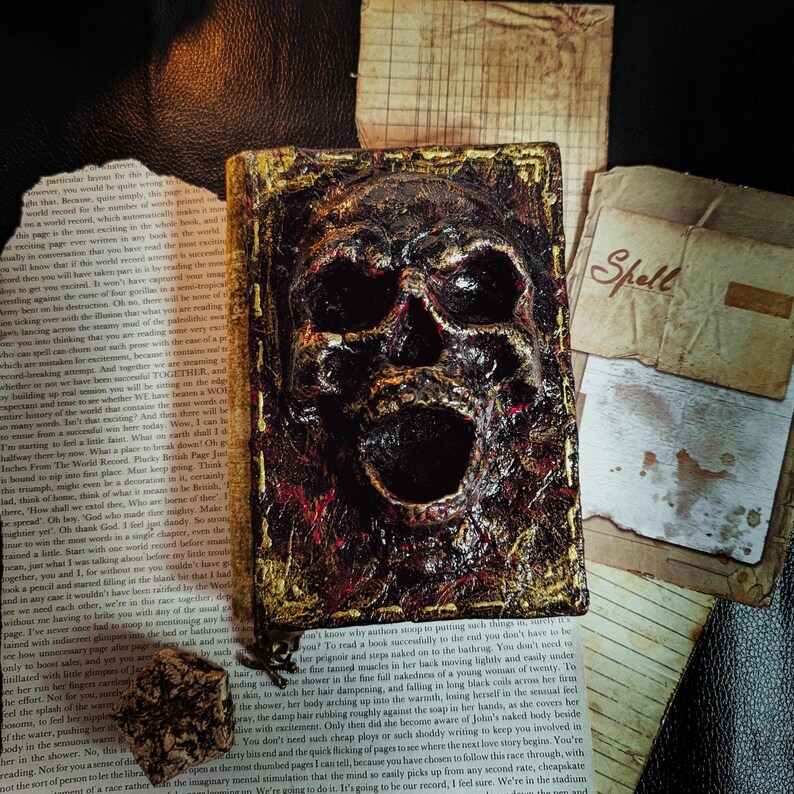 Occult spellbook with sculpted skull face cover, horror-style design on vintage papers