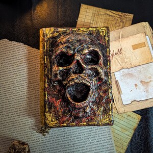 Occult spellbook with sculpted skull face cover, horror-style design on vintage papers