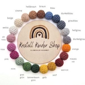 Könnte beinhalten: Ein Holz-Kreis mit einem Regenbogen-Design und dem Text "Kristall Kinder Shop". Der Kreis ist umgeben von gehäkelten Kugeln in verschiedenen Farben, darunter beige, weiß, rosa, rot, orange, gelb, grün, blau und grau. Jede Kugel ist mit einem deutschen Farbnamen beschriftet.
