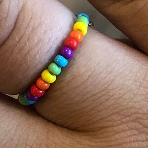 Pu&ograve; includere: Un anello di perline arcobaleno con una fascia argentata. Le perline sono piccole e rotonde e sono disposte nell'ordine dell'arcobaleno.