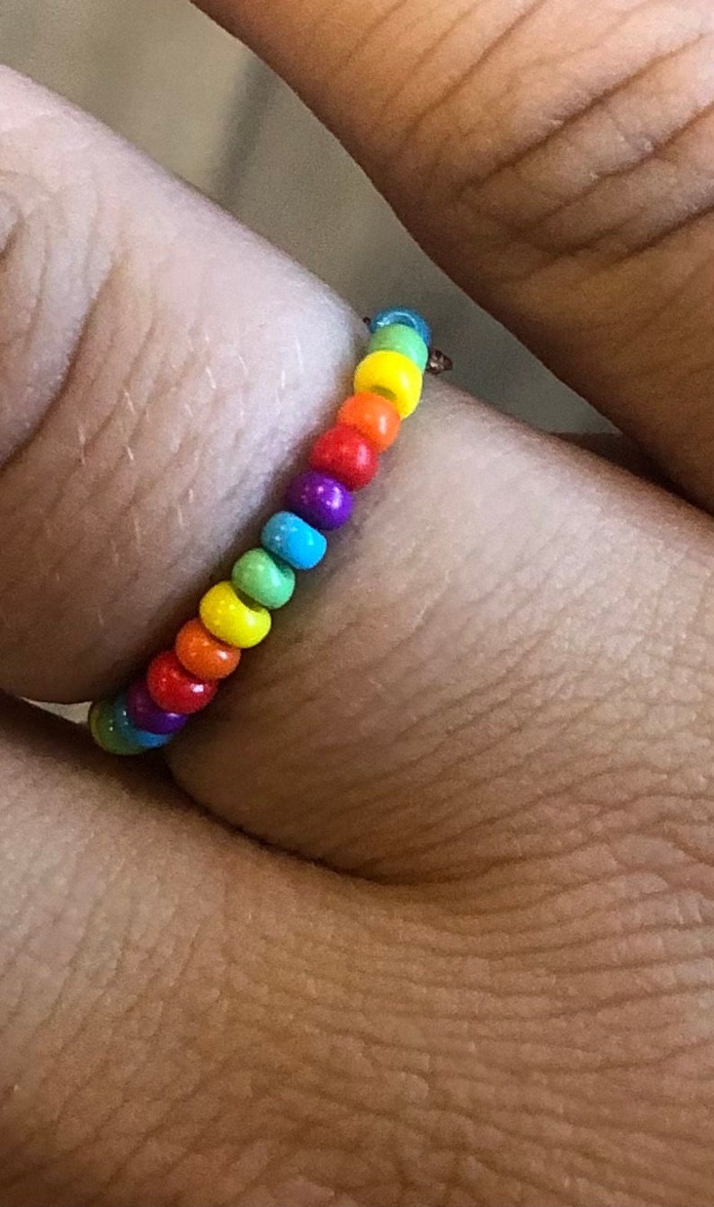 Pu&ograve; includere: Un anello di perline arcobaleno con una fascia argentata. Le perline sono piccole e rotonde e sono disposte nell'ordine dell'arcobaleno.