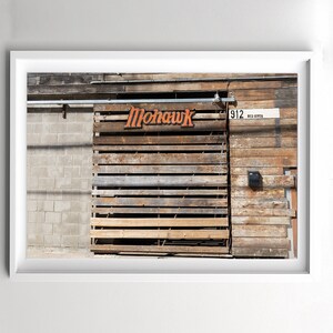 May include: A wooden building with a sign that says "Mohawk" in orange letters. The building has a wooden door with a metal grate over it. There is a sign above the door that says "912 RED RIVER".