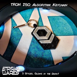 May include: A black and translucent white Tron ISO Algorithm keychain featuring a hexagonal geometric design with a metal ring. The text TRON ISO ALGORITHM KEYCHAIN is printed at the top, and EMPYRAE WARES 3 STYLES, GLOWS IN THE DARK! is at the bottom.