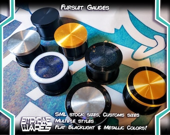 May include: A collection of circular ear gauges in various finishes including matte black, metallic gold, and silver. Some feature holographic blue centers with star accents. Text reads Fursuit Gauges, SML stock sizes, customs sizes, multiple styles, flat blacklight & metallic colors, and Empyrae Wares.