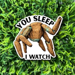 May include: A sticker featuring a brown, robotic-looking creature with blue accents. The text "YOU SLEEP I WATCH" is printed in a black, bold font around the creature. The sticker is set against a background of green foliage.