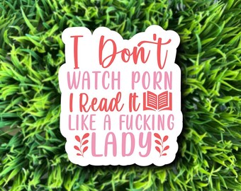 May include: A white sticker with the text "I Don't Watch Porn I Read It Like A Fucking Lady" in pink and red lettering. The sticker features a book graphic and decorative floral elements.