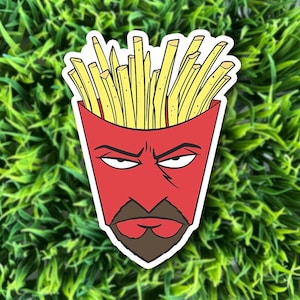 May include: A die-cut sticker featuring a red container filled with yellow french fries. The container has a stylized face with a brown goatee, a sharp jawline, and narrow, skeptical eyes, creating a character-like appearance with a bold outline.