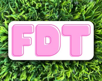 May include: A white sticker with the letters "FDT" in pink, outlined in white. The sticker is on a green background.