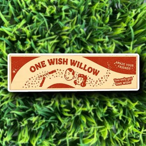 May include: A rectangular sticker with a vintage design. The sticker features the text "ONE WISH WILLOW" in a retro font, along with illustrations of a boy and girl. Additional text reads "AMAZE YOUR FRIENDS!" and "You only get ONE WISH!"