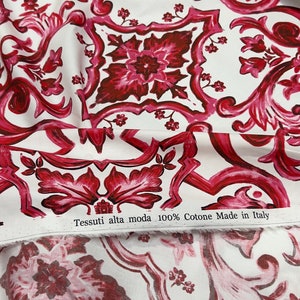 May include: White fabric with a red and pink floral pattern. The fabric has a label that reads "Tessuti alta moda 100% Cotone Made in Italy".