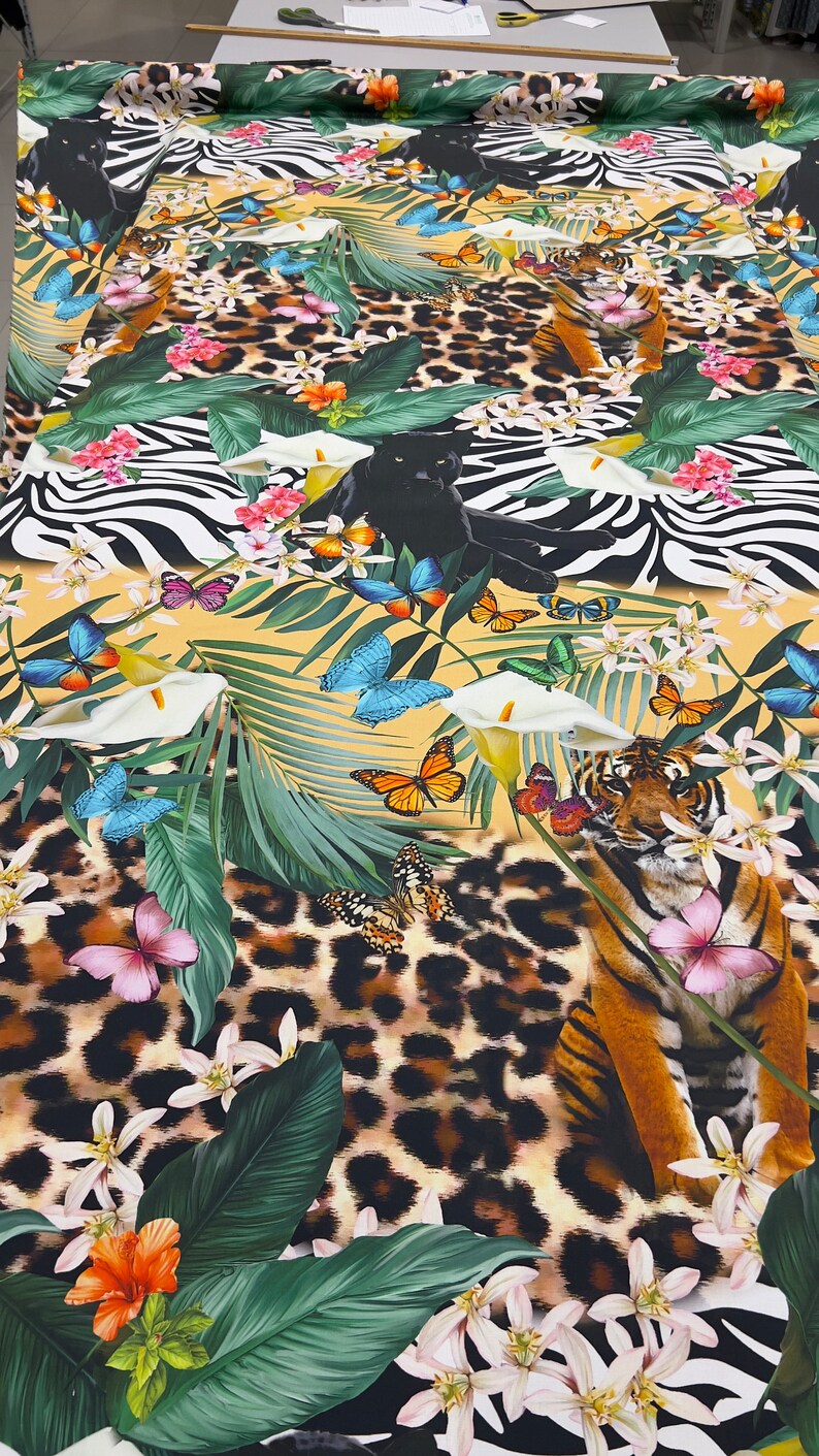 K&ouml;nnte beinhalten: Ein farbenfroher Stoff mit einem Dschungel-Druck, der schwarze Panther, Tiger, Schmetterlinge und tropische Pflanzen auf gelbem Hintergrund zeigt.