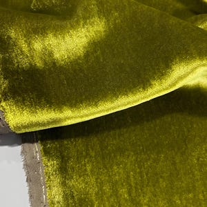 May include: Close-up of a soft, green velvet fabric with a subtle sheen. The fabric is folded and draped, showcasing its texture and drape.