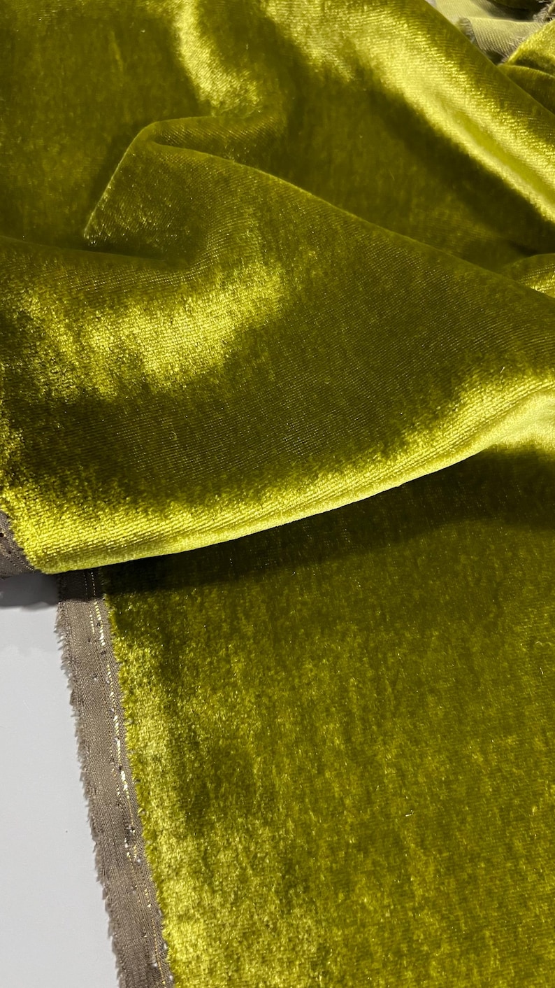May include: Close-up of a soft, green velvet fabric with a subtle sheen. The fabric is folded and draped, showcasing its texture and drape.