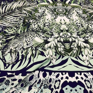 Op de afbeelding: Stof met een jungle-thema print. Het ontwerp toont een luipaard, tropische bladeren en zebra strepen in tinten groen, wit en marineblauw. Het patroon herhaalt zich over de stof, waardoor een visueel rijk en gedetailleerd textiel ontstaat.