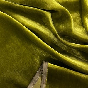 May include: Close-up of a soft, green velvet fabric with a subtle sheen. The fabric is folded and draped, showcasing its texture and drape.
