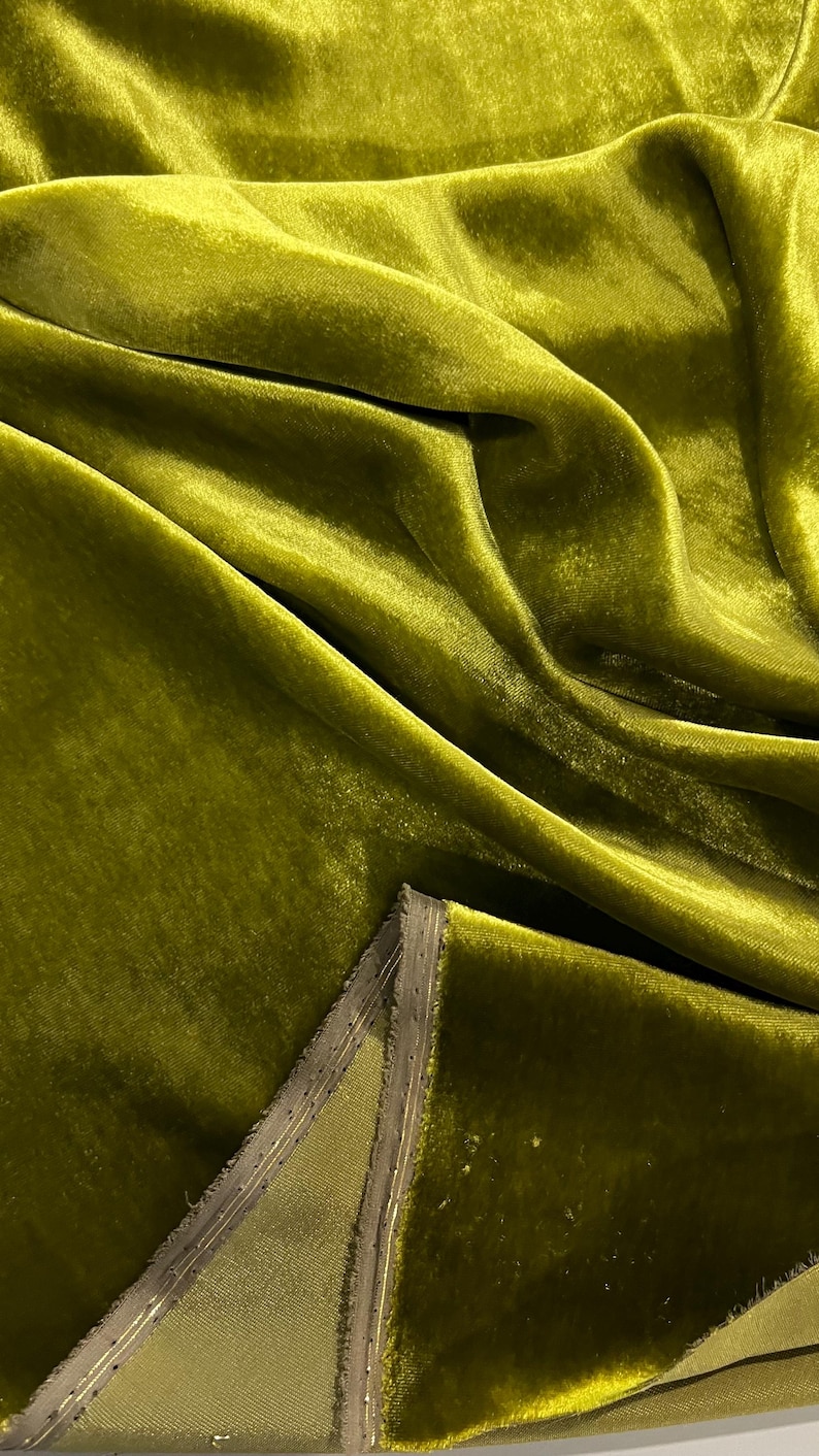 May include: Close-up of a soft, green velvet fabric with a subtle sheen. The fabric is folded and draped, showcasing its texture and drape.