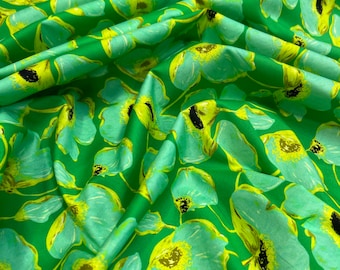May include: Green fabric with a light blue floral pattern. The flowers have yellow centers and black accents.